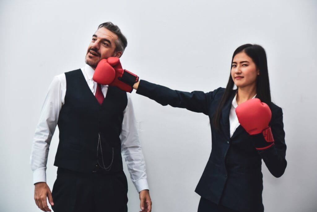 Office Worker Wearing Boxing Gloves Punching Her Colleague Depicting Workplace Bullying