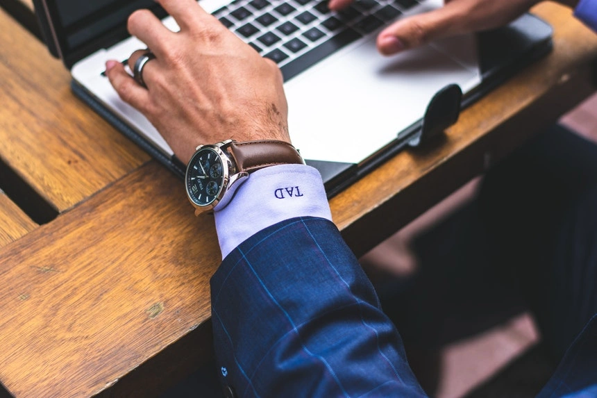 a man wearing a watch and typing a follow up e mail to pursue his job application