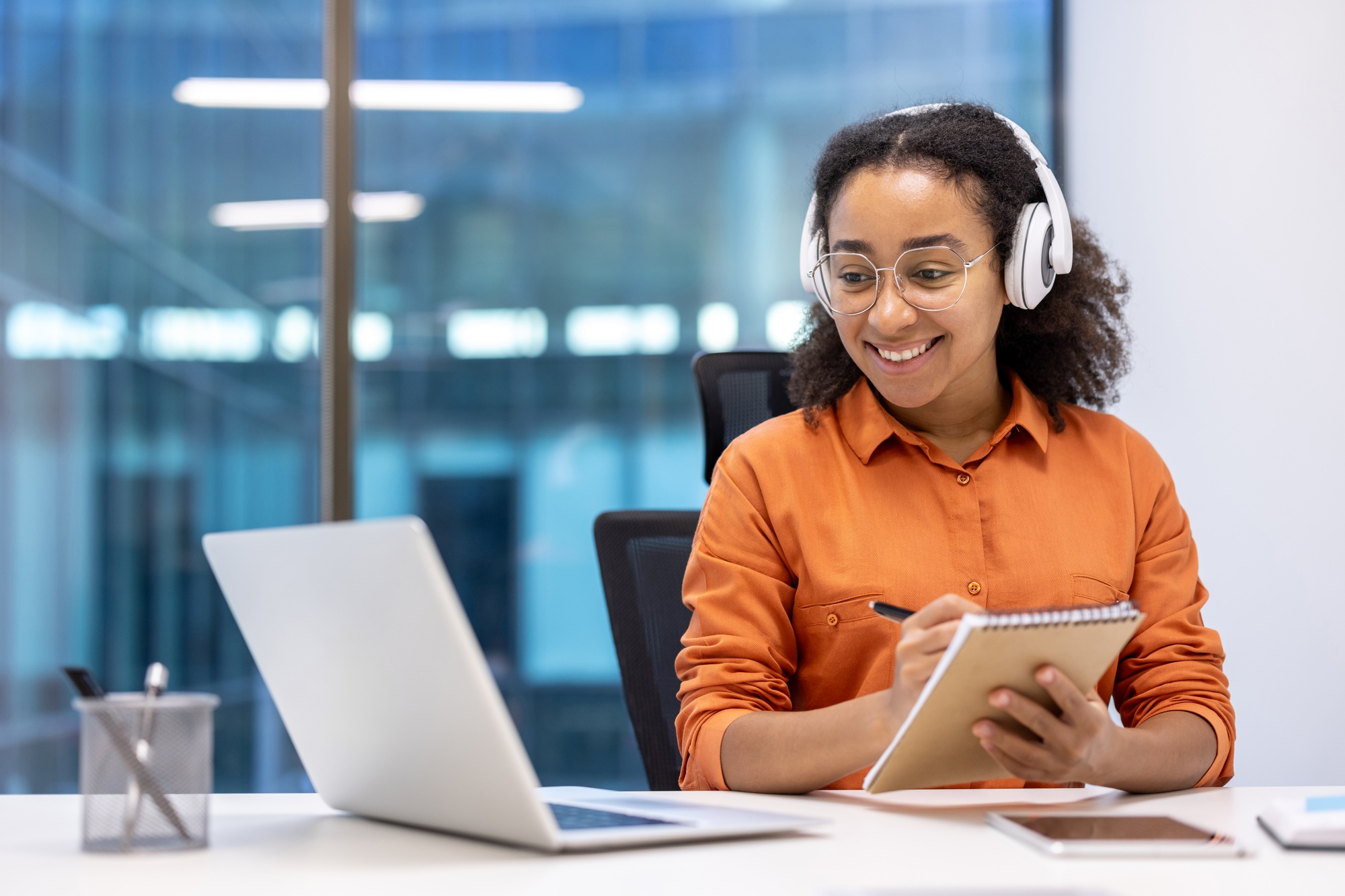 Young woman enjoying learning at workplace with laptop and notepad. Smiling while wearing