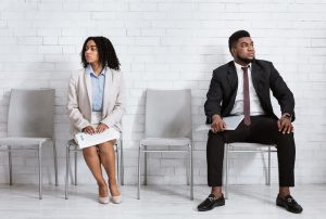 Black man and woman in formal wear looking in opposite directions, feeling competitive while waiting for job interview at office lobby. Vacancy fair, staff recruitment concept