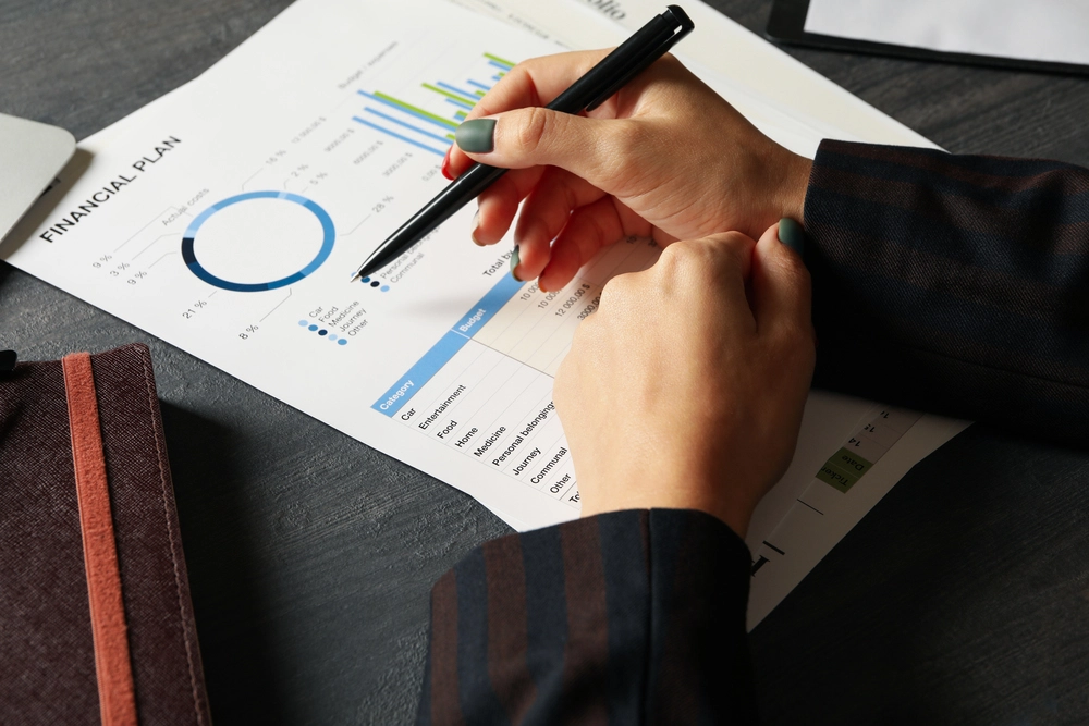 A Hand With Pen Pointed To A Financial Plan Document