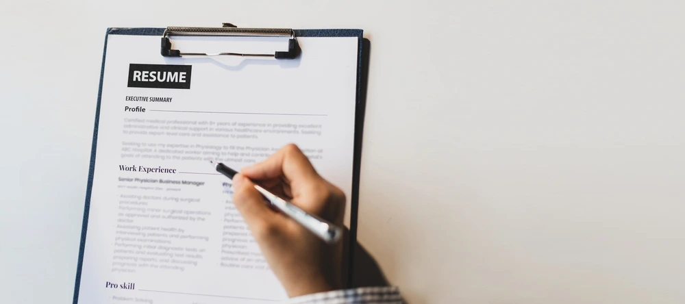 A Top View Of A Resume With A Hand Holding A Pen On Top Of It