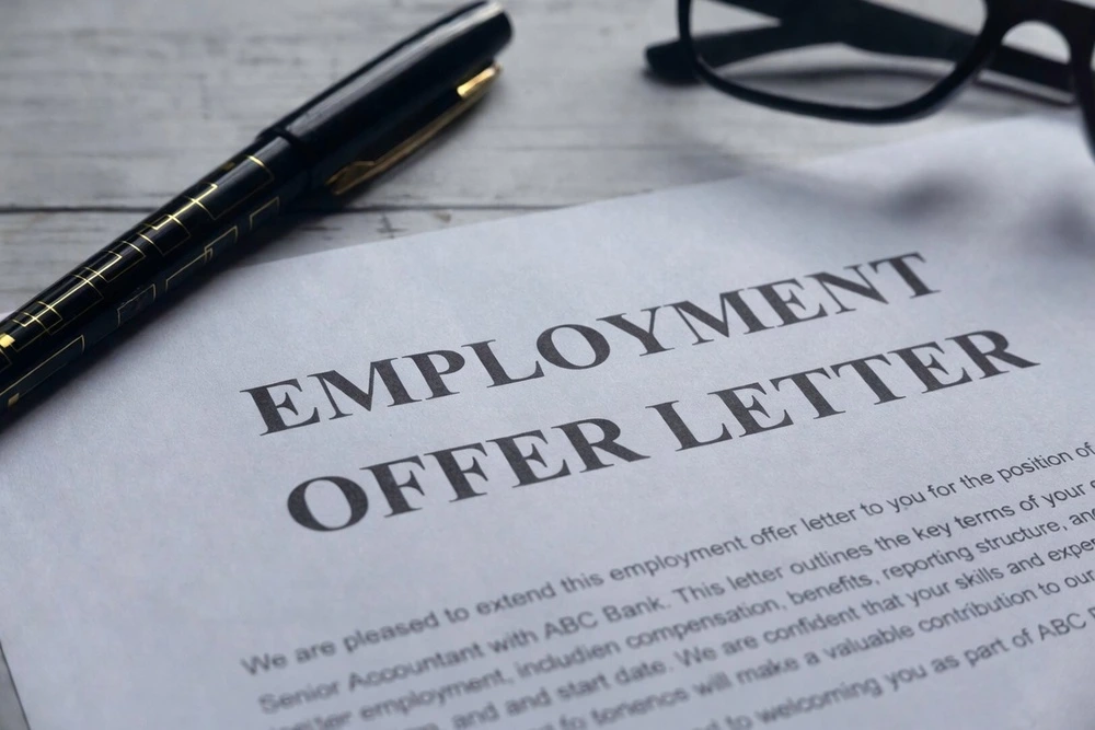 Employment Offer Letter Placed Neatly On A Desk With A Pen And Reading Glasses Resting On Top.