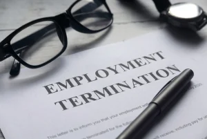 An overhead shot shows a piece of paper stating "Employment Termination" next to a pen, glasses, and watch.