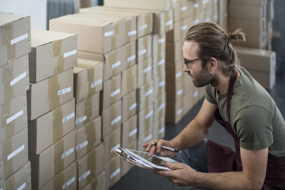 A Sales Associate Using Digital Tablet To Check Boxed Products Inventory In A Storeroom