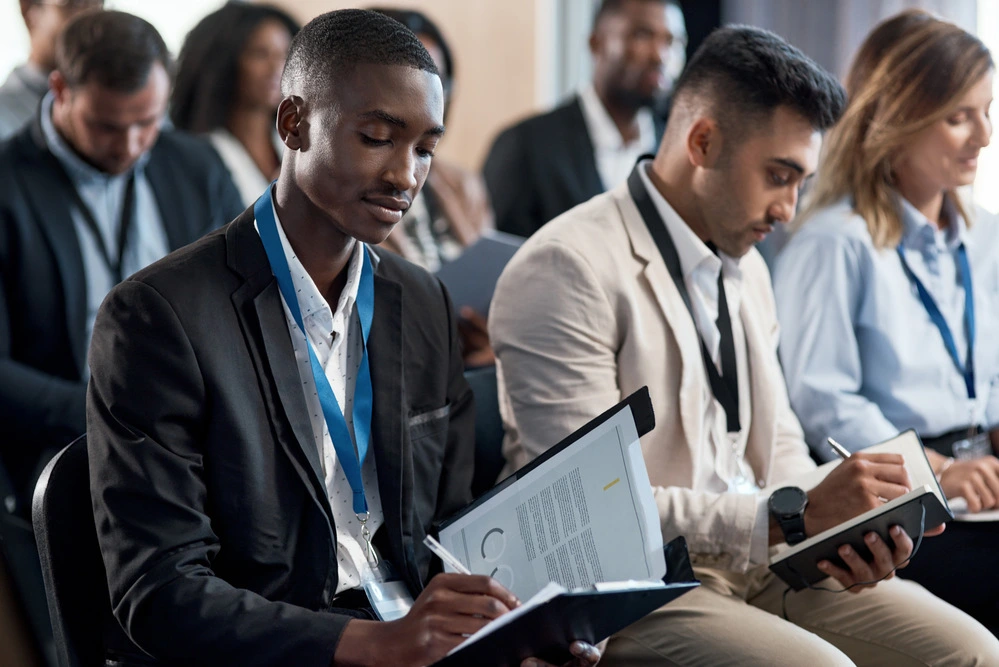 A Jobseeker Documenting Recruiter Names, Job Titles, And Notes During Discussions At A Job Fair.