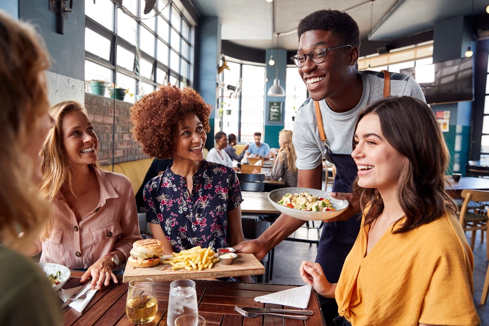 A Restaurant Staff Happily Serving Guests Leveraging Hard And Soft Skills In Accomplishing Server Duties